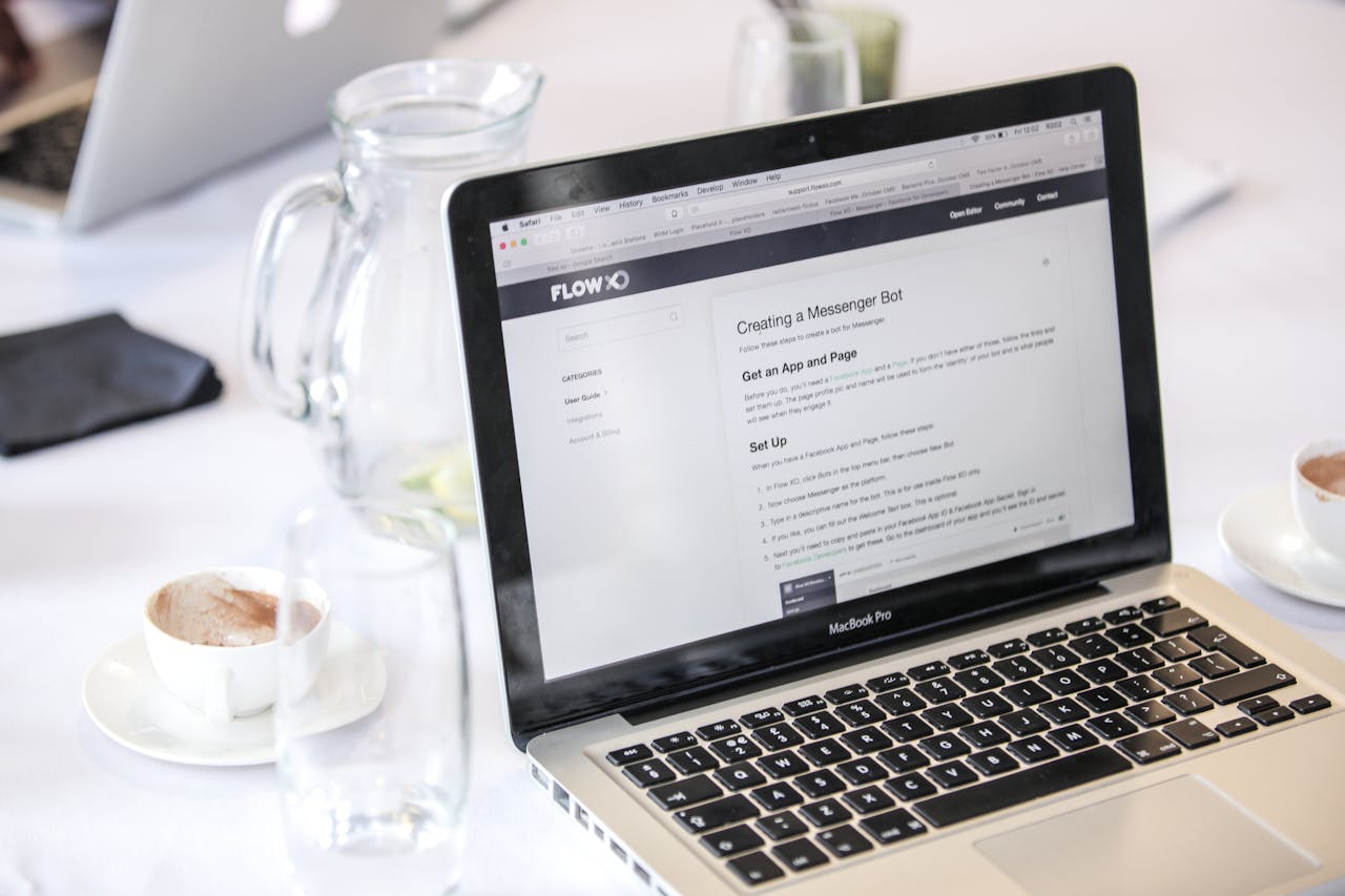 Close-up of a MacBook Pro displaying a webpage, with coffee cups and water pitcher on a table.